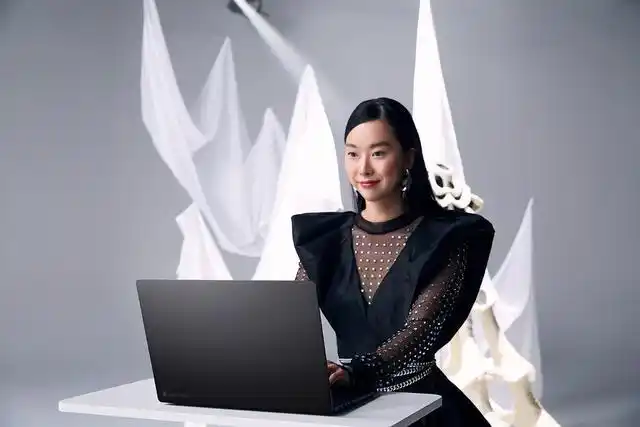 Woman in stylish black outfit working on ASUS ProArt laptop at a modern creative studio setup