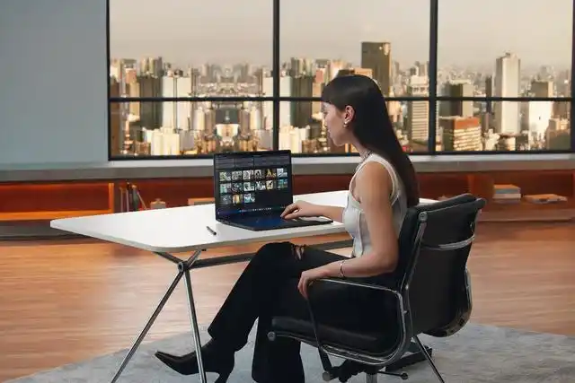 Woman working on a laptop in a modern office with a city skyline view in the background
