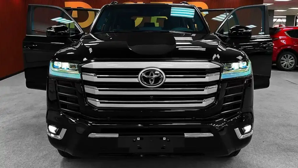 Front view of the 2025 Toyota Land Cruiser in black with LED headlights and bold chrome grille on display indoors