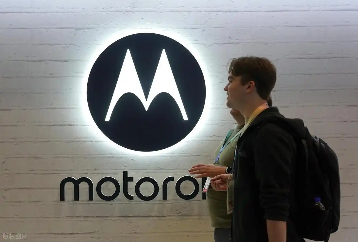 A person stands next to a large, illuminated Motorola logo