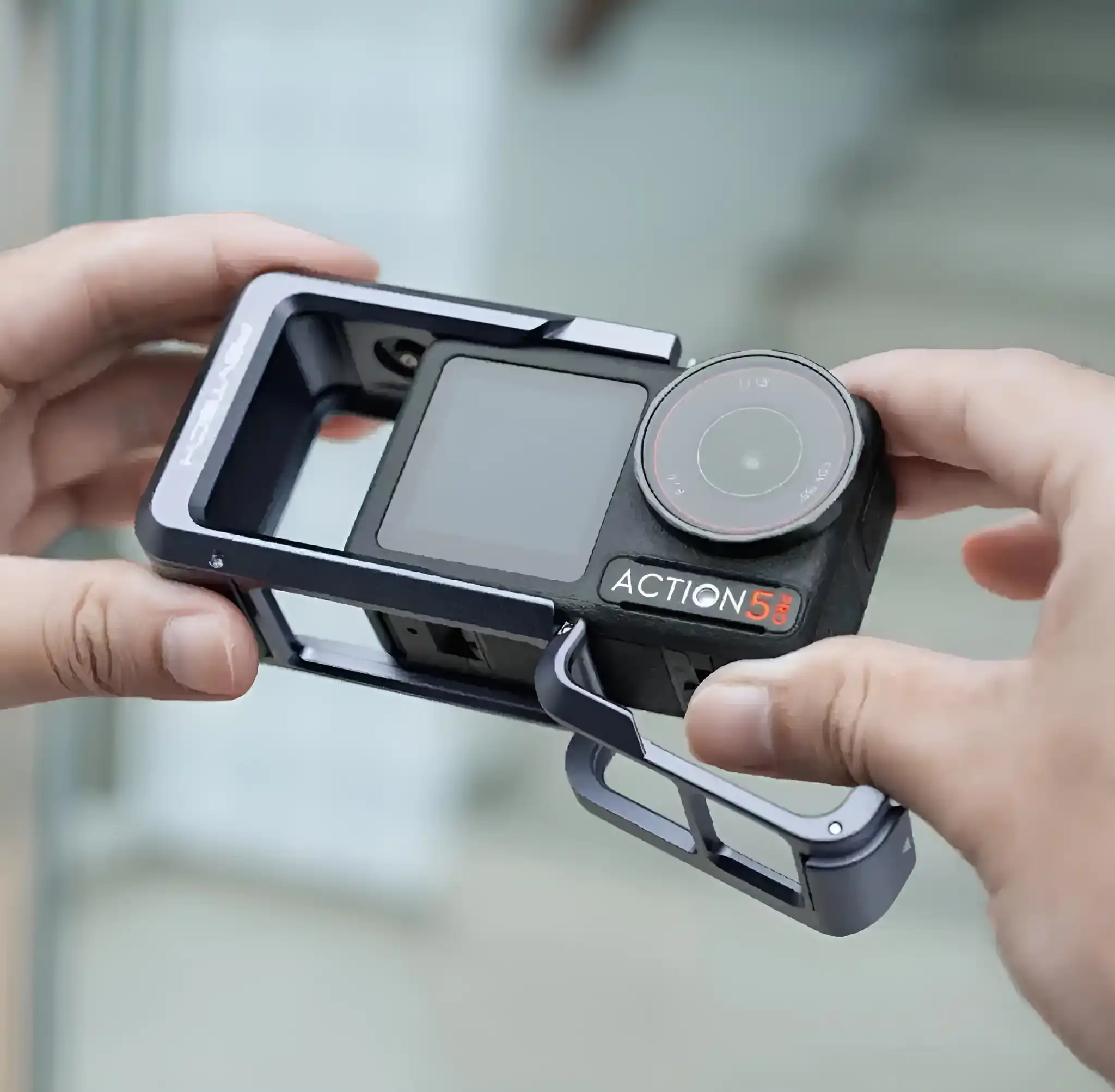 A person's hands holding the DJI Osmo Action 5 camera, which is being placed inside a gray PGYTECH protective frame.