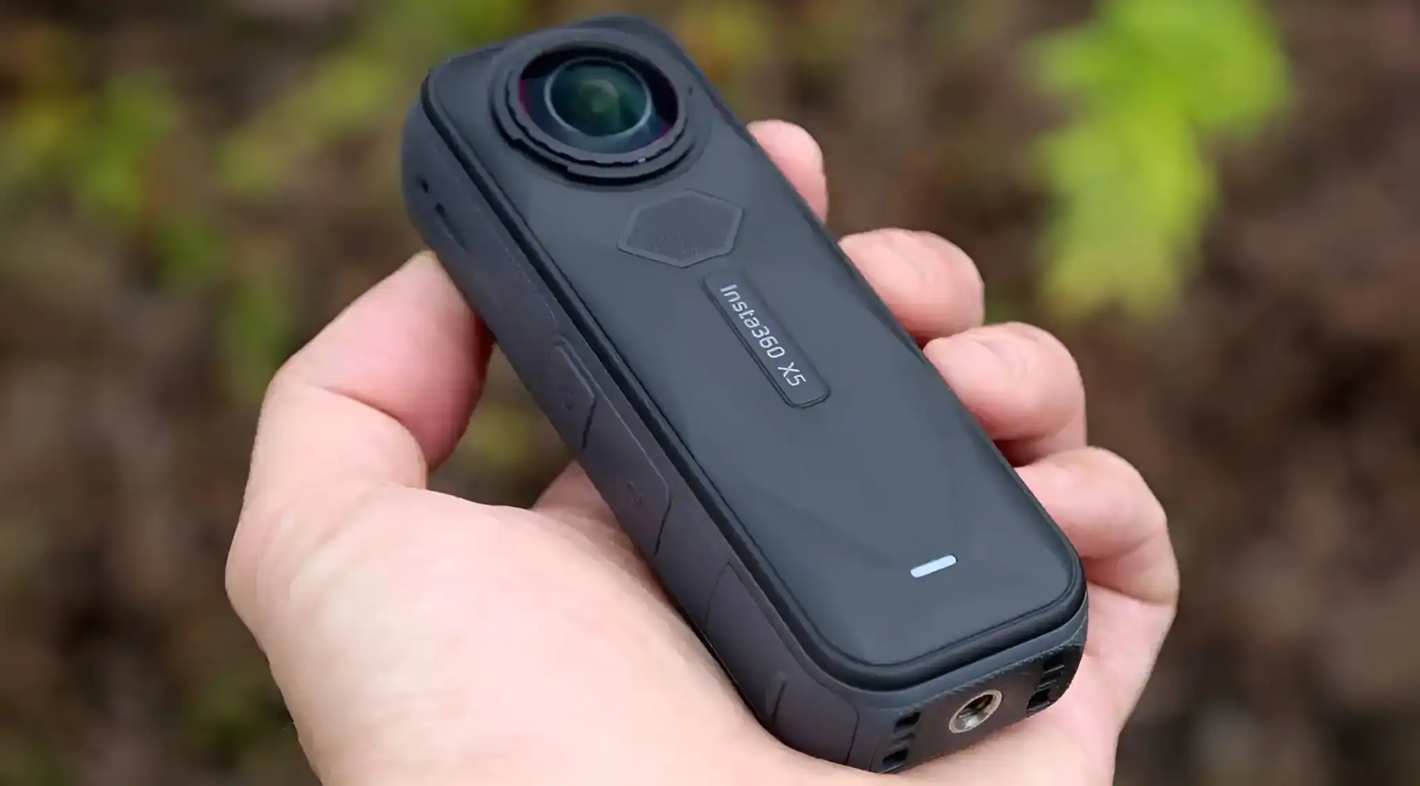A person's hand holds the black, rectangular Insta360 X5 camera with its distinctive twin lenses.