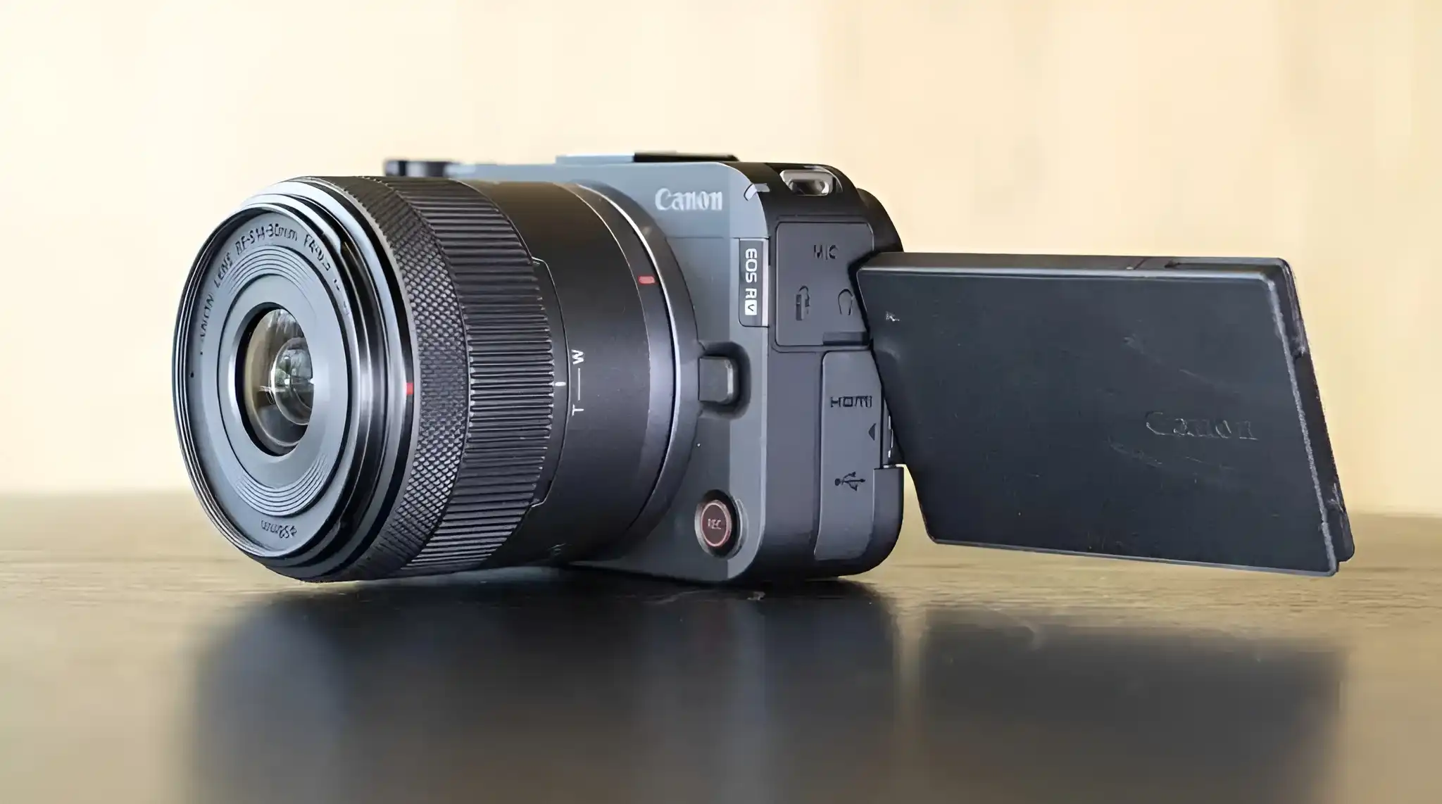 A Canon EOS R50 camera, with its vari-angle screen flipped out, sits on a black reflective surface.