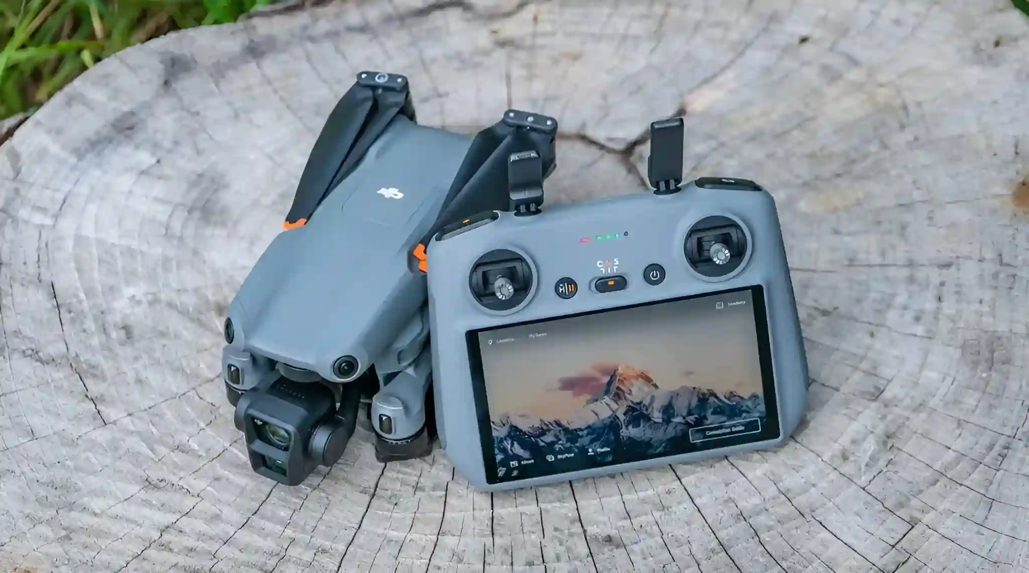 A DJI Air 3 drone and its remote controller with an attached screen sit on a textured tree stump.
