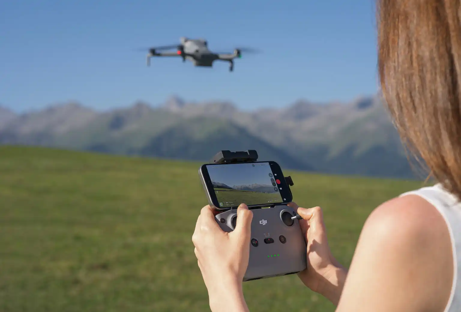 Person flying DJI Mini 5 Pro drone with remote controller and smartphone display in scenic mountain field